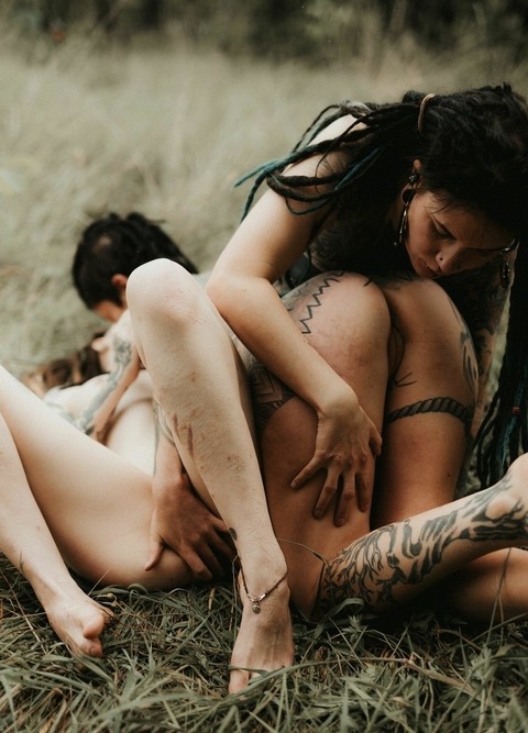 Three tattooed girls share lesbian kisses in long grass near a fir tree | Фото 1