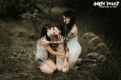 Three tattooed girls share lesbian kisses in long grass near a fir tree | Фото 12