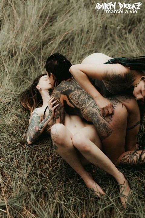 Three tattooed girls share lesbian kisses in long grass near a fir tree | Фото 15