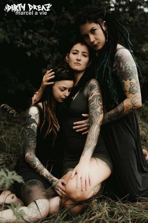 Three tattooed girls share lesbian kisses in long grass near a fir tree | Фото 3