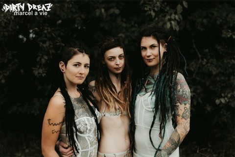 Three tattooed girls share lesbian kisses in long grass near a fir tree | Фото 4