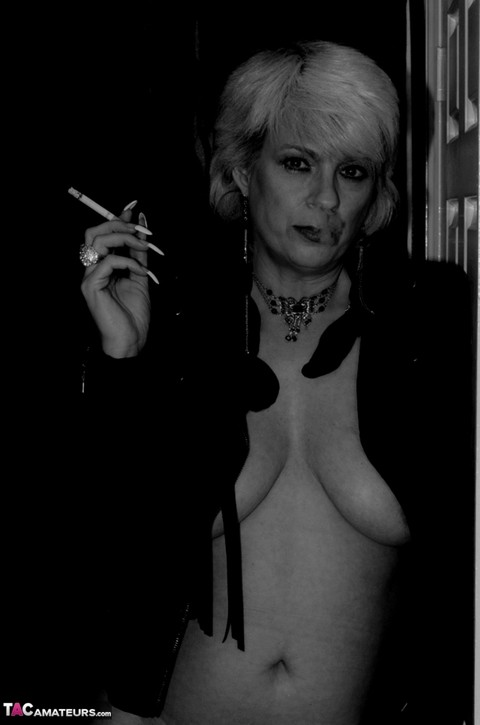 Older blonde lights a cigarette while showing her bare breasts and pussy | Фото 9