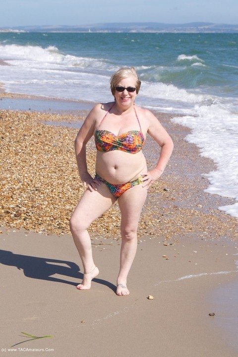 Mature UK woman Speedy Bee wears sunglasses while getting naked at the beach | Фото 1