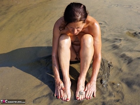 Naked older woman Diana Ananta covers her feet in beach sand at low tide | Фото 11