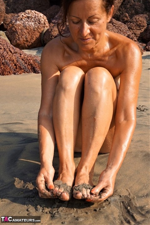 Naked older woman Diana Ananta covers her feet in beach sand at low tide | Фото 7