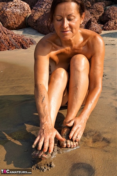 Naked older woman Diana Ananta covers her feet in beach sand at low tide | Фото 8