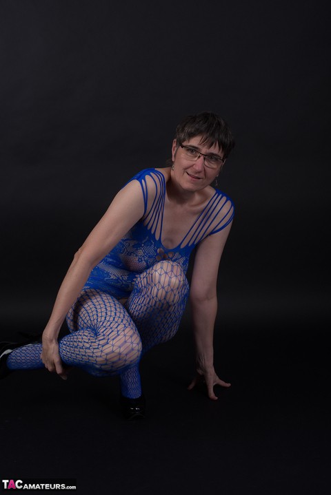 Older model poses in a crotchless bodystocking and heels with her glasses on