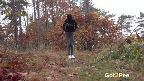 Clothed girl pulls down her pants to take a piss on a path thru the woods