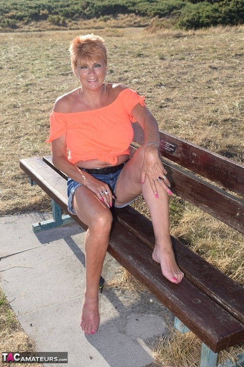 Mature redhead Dimonty shows her tits on a bench in a country field | Фото 13