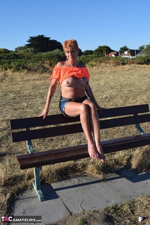 Mature redhead Dimonty shows her tits on a bench in a country field | Фото 18