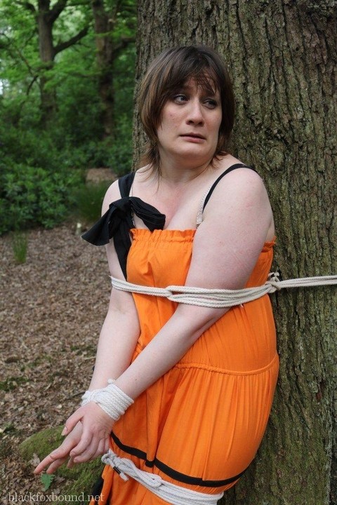 Fat female is gagged and tied to a tree in the woods with her clothes on