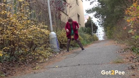 Caucasian female Lora takes a piss while walking on a pathway in the city