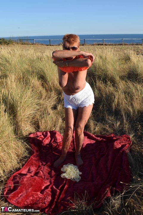 Fit older lady Dimonty exposes big naturals on a blanket overlooking the ocean