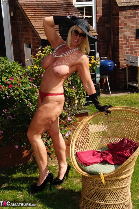 Blonde MILF displays her large tits in a big hat and gloves while in a yard | Фото 17