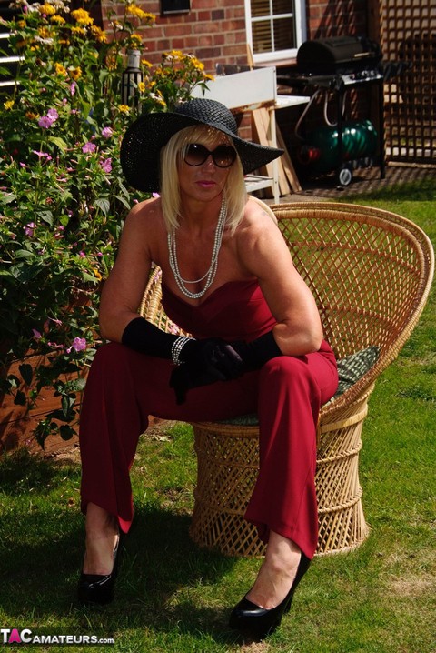 Blonde MILF displays her large tits in a big hat and gloves while in a yard | Фото 4