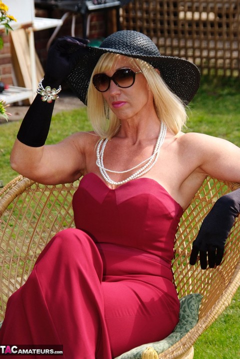 Blonde MILF displays her large tits in a big hat and gloves while in a yard