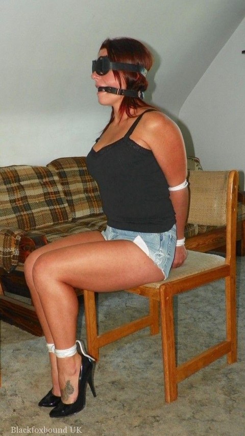 Redhead is gagged while cuffed and hogtied on a futon in denim shorts