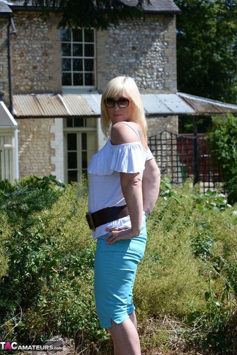 Middle-aged blonde Melody models in a bra while in a backyard