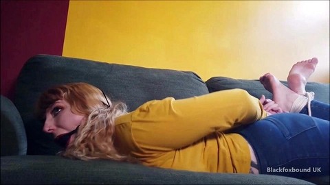 Barefoot white girl is hogtied on a sofa while ball gagged in her clothing | Фото 3