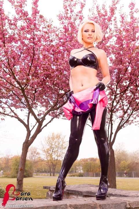 Blonde Lara Larsen unzips a latex dress to expose a matching bra in a park