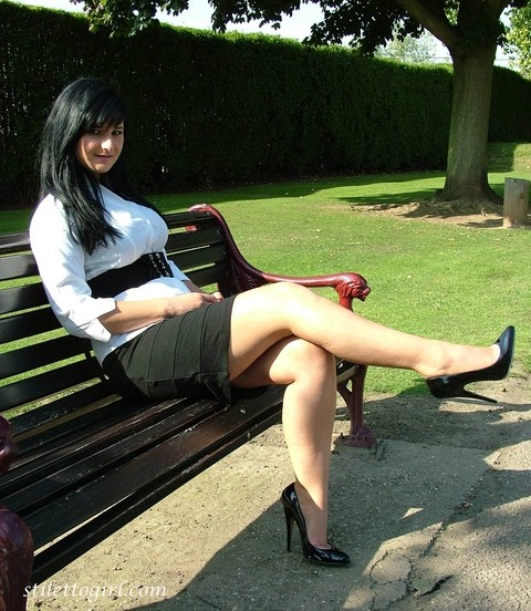 Dark haired female displays some leg and her stiletto heels on a park bench | Фото 5