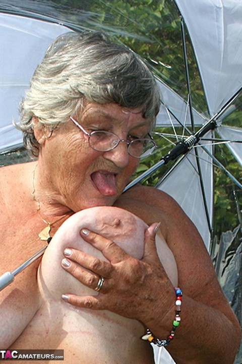 Obese oma Grandma Libby holds an umbrella while posing naked by fir trees | Фото 18