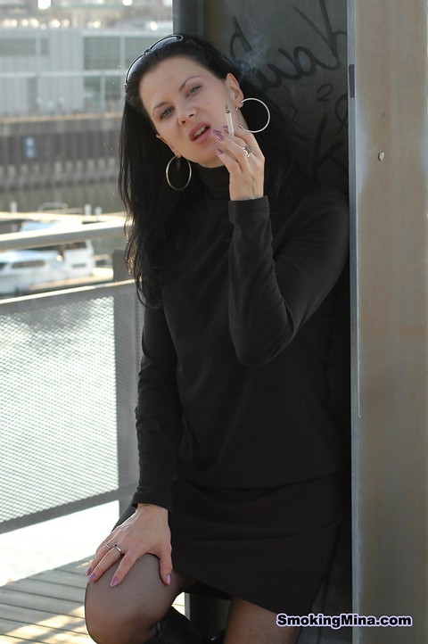 Fully clothed brunette lights up a cigarette with her sunglasses atop her head