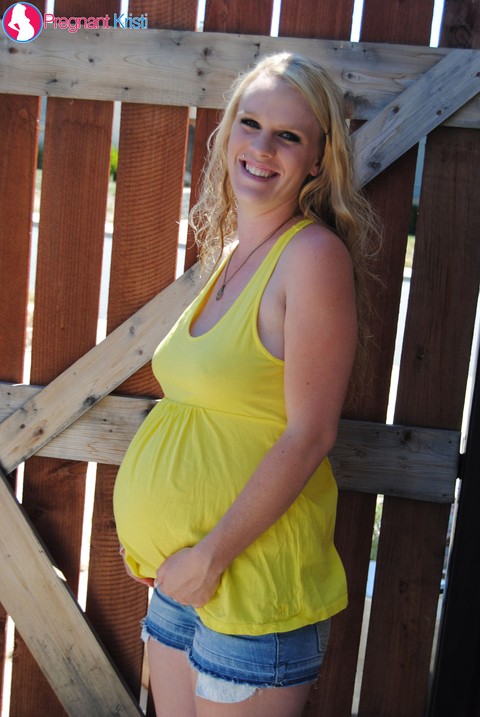 Pregnant blonde amateur Kristi shows her swollen tits and belly by a gate