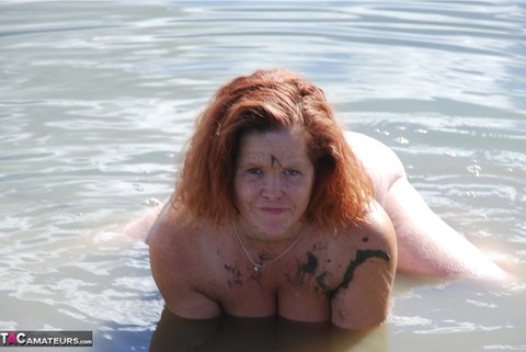 Redheaded amateur Misha covers her big tits in mud while in shallow water | Фото 11