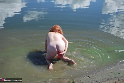 Redheaded amateur Misha covers her big tits in mud while in shallow water | Фото 17